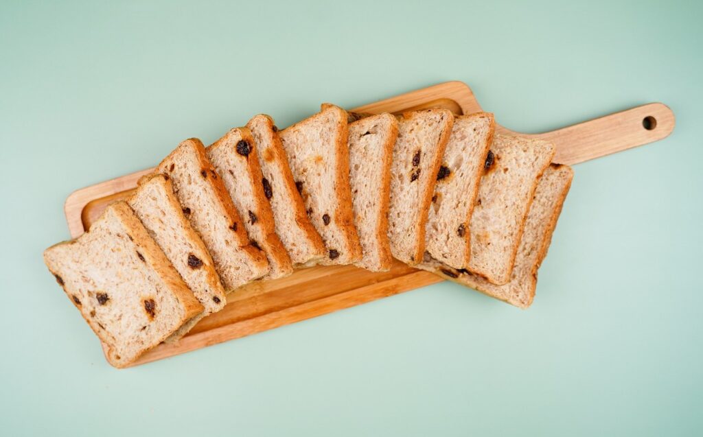 Gardenia Wheat Raisin Loaf placed on a wooden cutting board with light blue background